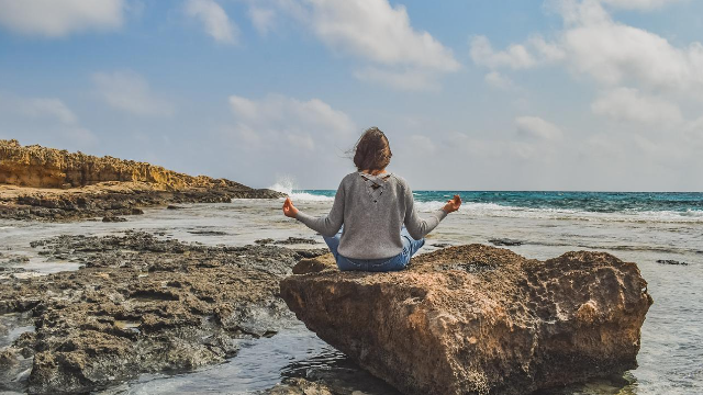 Woman Sitting on a Rock In A Meditation Position Facing the Ocean